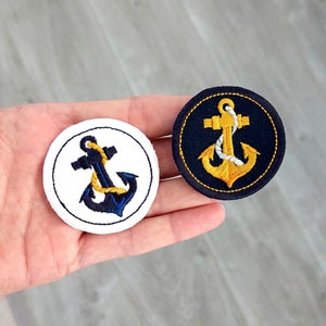 Könnte beinhalten: Zwei gestickte Bügelbilder mit Ankermotiven. Ein Patch ist weiß mit einem blauen Anker und einem gelben Seil. Der andere Patch ist schwarz mit einem gelben Anker und einem weißen Seil.