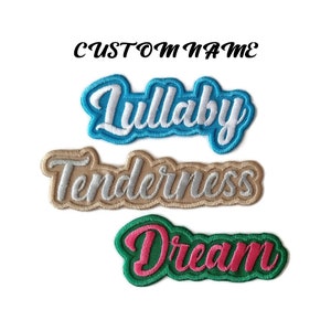 Può includere: Tre toppe ricamate con le parole "Lullaby", "Tenderness" e "Dream". Le toppe sono di diversi colori: blu, beige e verde.