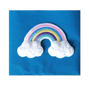 Può includere: Una toppa ricamata raffigurante un arcobaleno colorato che si inarca tra due nuvole bianche e soffici. L'arcobaleno è composto da bande concentriche rosa, azzurre, gialle, viola e verde acqua, il tutto delineato da un bordo bianco su sfondo blu.