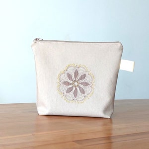May include: A beige zippered pouch with a brown and gold embroidered mandala design.