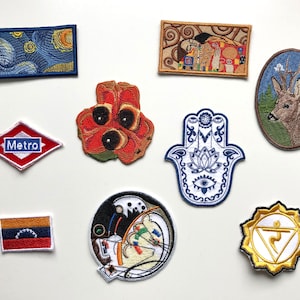 May include: A collection of embroidered patches with various designs. Included are patches depicting a starry night scene, a deer in an oval frame, a red and white Metro sign, a red flower, a Hamsa hand, a flag, a circular art piece, and a yellow chakra symbol.