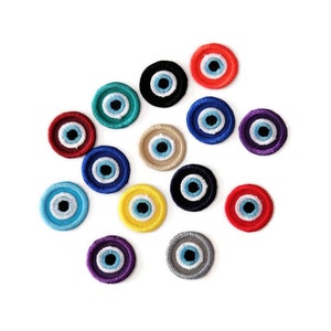 May include: Assortment of colourful round evil eye charms with blue and white centres. The charms are made of fabric and have a stitched design.