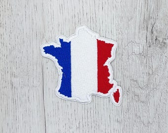 May include: A white fabric patch in the shape of France with the French flag colors, blue, white, and red, embroidered on it.