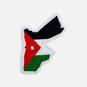 May include: Embroidered patch in the shape of Jordan, displaying the Jordanian flag. The flag design incorporates red, white, green, and black, with a white seven-pointed star on the red triangle. The patch has a white border.