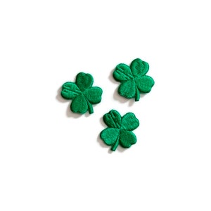 May include: Three green four-leaf clover patches. The patches are made of fabric and have a stitched design.