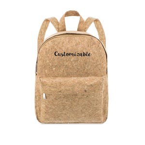 Könnte beinhalten: Ein hellbrauner Kork-Rucksack mit einer Vordertasche und verstellbaren Trägern. Das Wort "Customizable" ist auf der Vorderseite des Rucksacks aufgedruckt. Der Rucksack hat einen Reißverschluss und einen silbernen Reißverschluss.