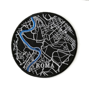 Könnte beinhalten: Ein gestickter schwarzer und weißer Aufnäher mit einer Karte von Rom, Italien. Der Tiber ist in Blau hervorgehoben. Das Wort "ROMA" ist in Weiß unter der Karte gestickt.