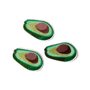 May include: Three embroidered avocado patches, each showing a halved avocado with a brown pit and green flesh. The patches are on a white background.