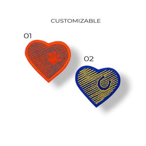Puede incluir: Dos parches en forma de corazón. Uno es naranja con una huella de pata, el otro es azul con una herradura. La palabra "CUSTOMIZABLE" está encima de los parches. Los parches están etiquetados "01" y "02".