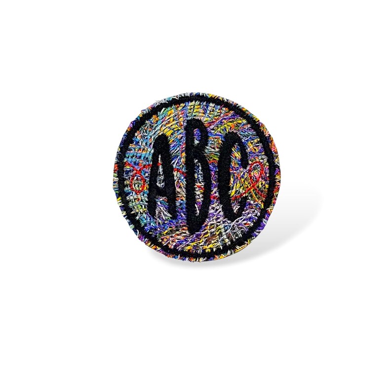 Pode incluir: Um patch redondo com um fundo tecido colorido. O patch apresenta as letras "ABC" em uma fonte preta em negrito. O patch tem uma borda costurada preta.