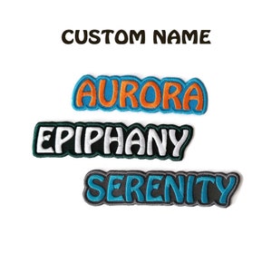 Op de afbeelding: Drie geborduurde strijklabels met de namen "Aurora", "Epiphany" en "Serenity" in kleurrijke letters. De labels zijn perfect om kleding, tassen of andere stoffen items te personaliseren.