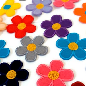 Puede incluir: Surtido de parches de flores de fieltro de colores con centros amarillos. Los parches son de varios colores, incluyendo rojo, azul, morado, rosa, gris y amarillo.