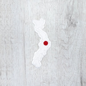 Puede incluir: Contorno de fieltro blanco del país de Vietnam con un círculo rojo en el centro, que representa la capital Hanoi, sobre un fondo de madera blanca.