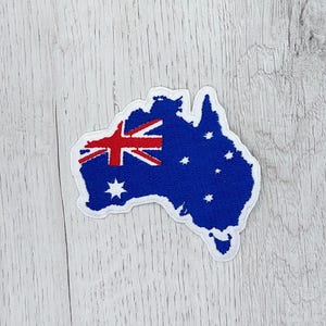 Könnte beinhalten: Ein weißer Filz-Aufnäher in Form der Umrisse Australiens mit einer rot-weiß-blauen australischen Flagge in der oberen linken Ecke und blauen Sternen auf dem Rest des Aufnähers.