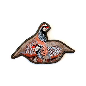 May include: Embroidered patch featuring two brown and gray partridges with red accents. The birds are perched on a green leafy branch.