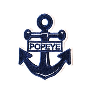 Könnte beinhalten: Blauer gestickter Bügel-Aufnäher mit einem Anker und dem Wort "POPEYE" auf einem weißen Banner.