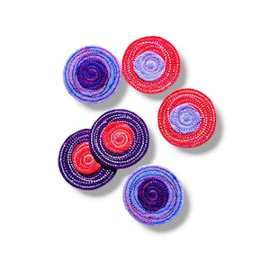 Puede incluir: Un conjunto de seis posavasos circulares con un diseño en espiral. Los colores incluyen rojo, morado y azul. Cada posavasos tiene aproximadamente 10 cm de diámetro.