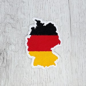 May include: An embroidered patch shaped like the outline of Germany with the German flag colors: black, red, and yellow.