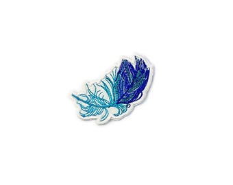 Könnte beinhalten: Ein gestickter Feder-Patch in Blau- und Türkistönen. Die Feder ist mit einer weißen Umrandung versehen und eignet sich perfekt, um Kleidung oder Accessoires einen Hauch von Verspieltheit zu verleihen.