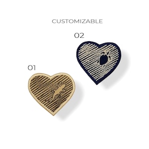 Könnte beinhalten: Zwei herzförmige Aufnäher. Einer ist beige mit einem Eidechsen-Design, der andere marineblau mit einer Schildkröte. Das Wort "CUSTOMIZABLE" steht über den Aufnähern, mit den Zahlen "01" und "02" neben jedem Aufnäher.