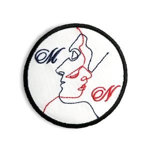 Può includere: Toppa ricamata con sfondo bianco, raffigurante due volti in un disegno a linea continua. I volti sono delineati con filo rosso e blu navy. Le lettere "M" e "N" sono ricamate in blu navy e rosso.