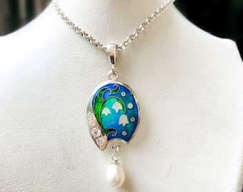 May include: A silver necklace with a pendant featuring a blue and green enamel design of lily of the valley flowers and a single pearl drop.