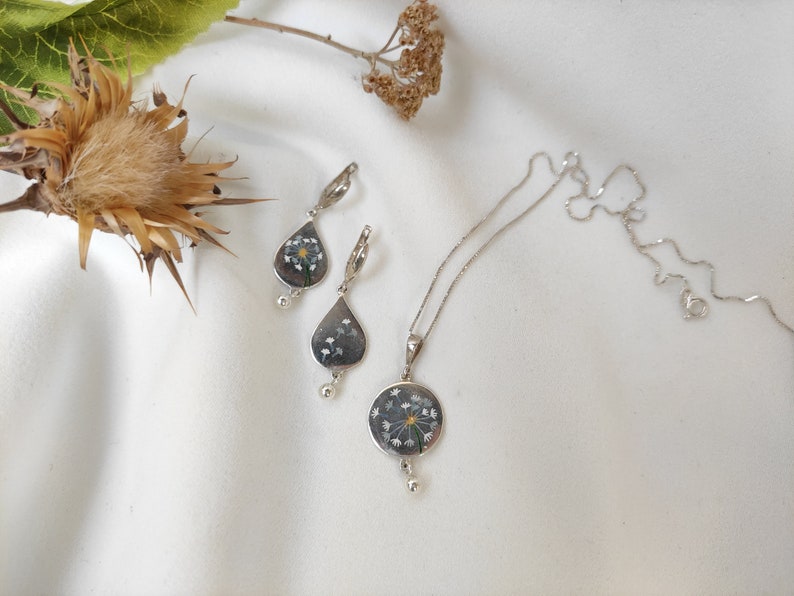May include: A silver necklace and earrings set with a delicate flower pendant and matching teardrop earrings. The flower pendant is made with real pressed flowers and has a silver chain.