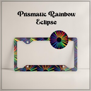 May include: A rectangular license plate frame featuring a vibrant, multi-colored radial sunburst pattern against a black background. The text 'Prismatic Rainbow Eclipse' is printed in a bold, dark, stylized font above the frame.
