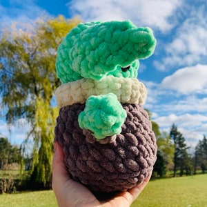 Peut inclure: Un jouet en peluche crochet&eacute; en forme de personnage extraterrestre vert. Le jouet a un corps brun, un col blanc et une t&ecirc;te verte avec de grands yeux. Le jouet est tenu dans la main d'une personne.