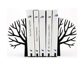 May include: Black metal bookends shaped like a tree with bare branches. The bookends are holding up five books with Turkish titles: "Ay hadi insallah...", "Akıl Tutulması", "Bir delilin hatıra defteri", "...", and "...".