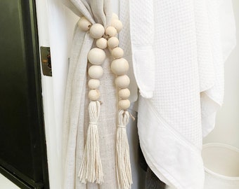 May include: White linen curtains with wooden bead tassels. The beads are strung together in a simple design and the tassels are made of natural fiber.