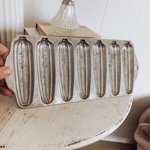 May include: A vintage metal baking pan with six individual molds shaped like long, thin corn dogs. The pan is silver and has a slightly worn look.
