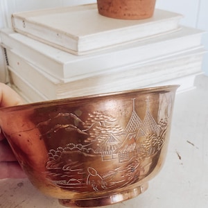 May include: A copper bowl with an etched design of a Japanese landscape. The bowl is round and has a wide rim.