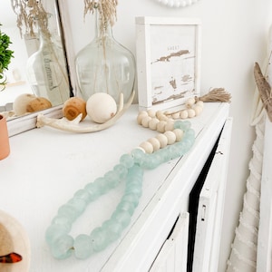May include: A white dresser with a light blue glass bead garland, a wooden bead garland, and a wooden sign that says "Sweet".