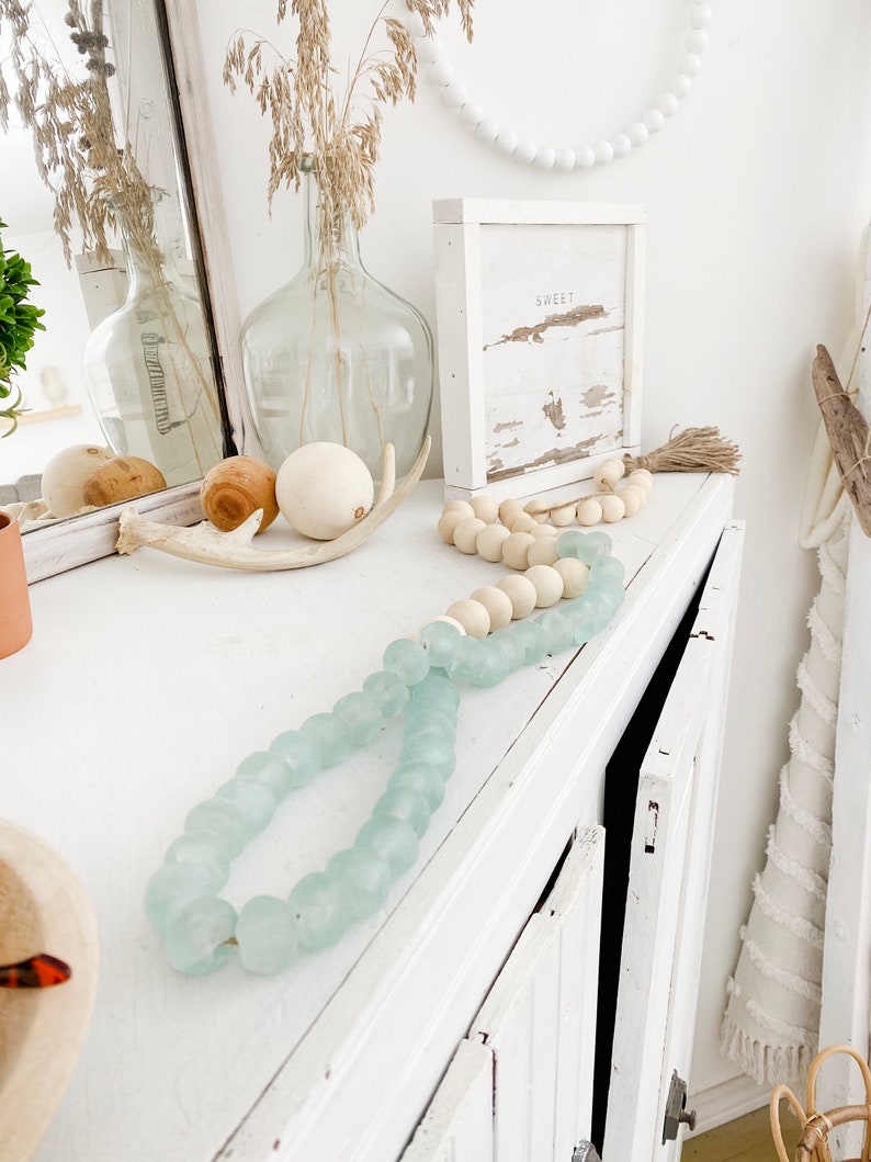 May include: A white dresser with a light blue glass bead garland, a wooden bead garland, and a wooden sign that says "Sweet".