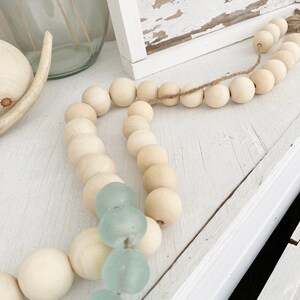 May include: A wooden bead garland with light blue glass beads interspersed throughout. The garland is draped over a white surface.