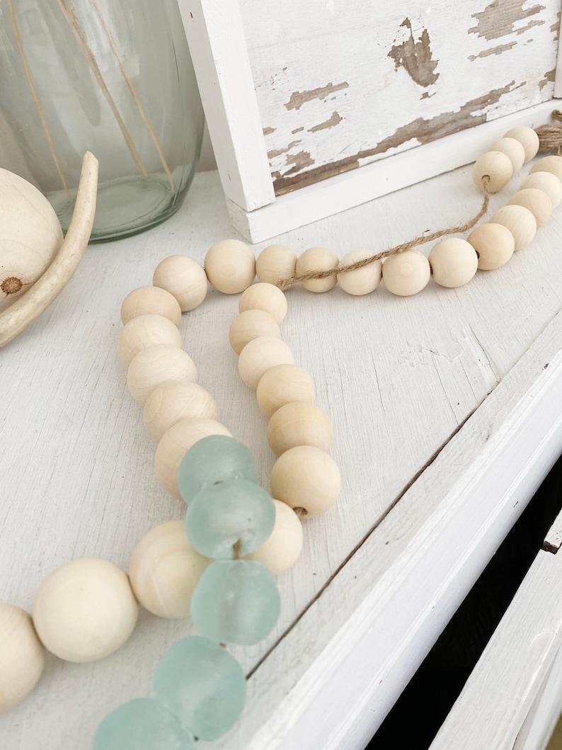 May include: A wooden bead garland with light blue glass beads interspersed throughout. The garland is draped over a white surface.