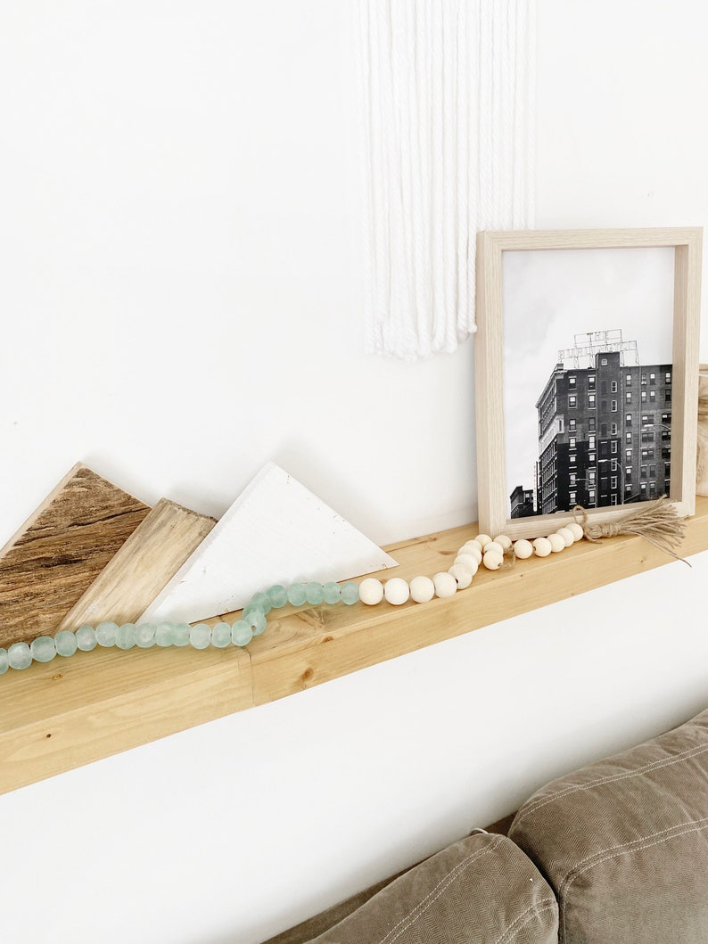 May include: A wooden shelf with a white and light brown geometric design, a black and white photo of a building, and a light blue and white beaded garland.