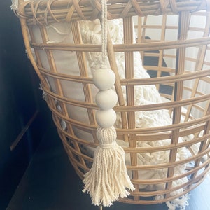 May include: A white tassel with three white wooden beads hanging from a woven wicker basket.