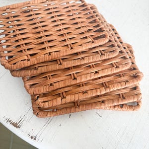 May include: A stack of four woven rectangular coasters in a warm brown hue. The coasters are made of a tightly woven material, creating a textured surface. The coasters are stacked on top of each other, showcasing their design and texture.