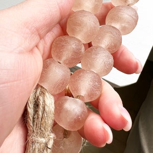 May include: A strand of translucent, light pink glass beads with a natural fibre tassel. The beads are round and have a slightly textured surface.