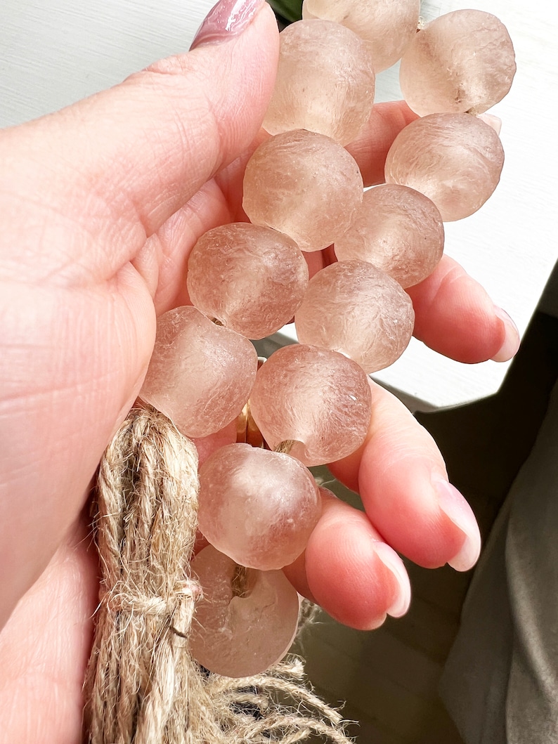 May include: A strand of translucent, light pink glass beads with a natural fibre tassel. The beads are round and have a slightly textured surface.