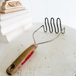 May include: A white ceramic mug with a black handle and the text "But First, Coffee" in a bold, black font. The mug is sitting on a wooden surface. The mug is approximately 4 inches tall.