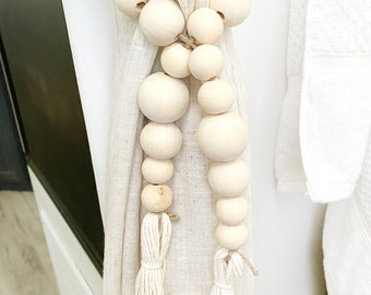 May include: White curtain tiebacks with wooden beads and tassels. The beads are strung on a natural twine cord and the tassels are made of white yarn.