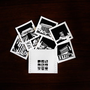 Puede incluir: Un conjunto de fotograf&iacute;as en blanco y negro de edificios, dispuestas en forma de abanico sobre una superficie de madera marr&oacute;n oscuro. Las fotograf&iacute;as est&aacute;n dispuestas alrededor de una tarjeta blanca con una cuadr&iacute;cula de nueve fotograf&iacute;as en blanco y negro m&aacute;s peque&ntilde;as.