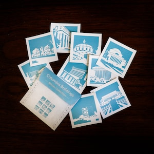 Puede incluir: Un conjunto de pegatinas azules y blancas con diferentes edificios del campus de la Universidad de Columbia. Las pegatinas est&aacute;n empaquetadas en un sobre blanco con el texto "Columbia Buildings Sticker Collection".