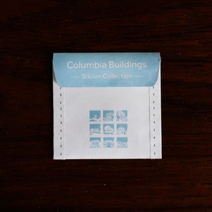 Puede incluir: Un sobre blanco con texto azul que dice "Columbia Buildings - Sticker Collection -" y presenta una cuadr&iacute;cula de nueve peque&ntilde;as im&aacute;genes de edificios.