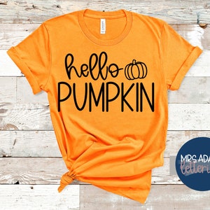 Peut inclure: T-shirt orange avec du texte noir qui dit "hello pumpkin" et un petit graphique de citrouille noire.