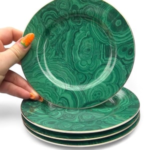 May include: A stack of three round plates featuring a vibrant green malachite pattern with swirling concentric rings and organic banding. Each plate has a smooth, glossy finish and a thin, metallic gold rim along the outer edge of the circular border.