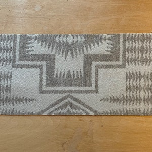 May include: A gray and white woven rug with a geometric pattern. The rug has a fringed edge.